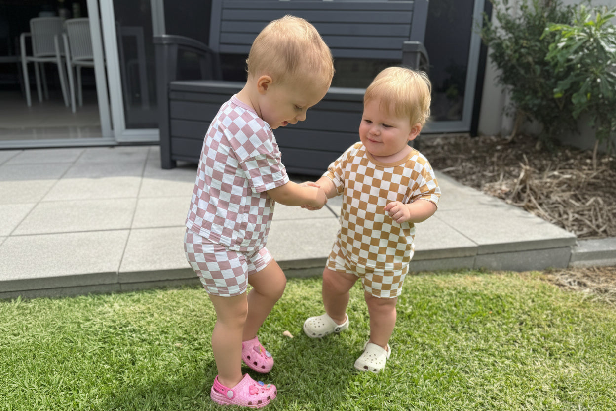 Two children in checkered outfits standing on grass outdoors.